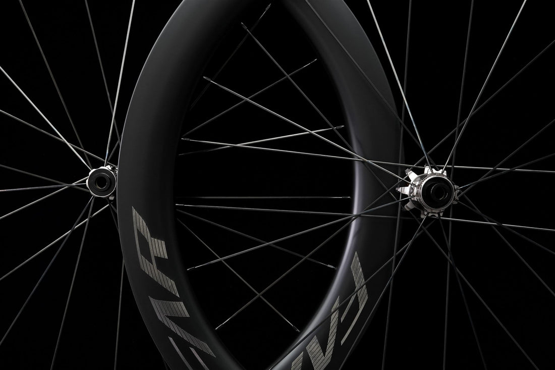 A carbon road wheel photographed on black, spokes and hub in view