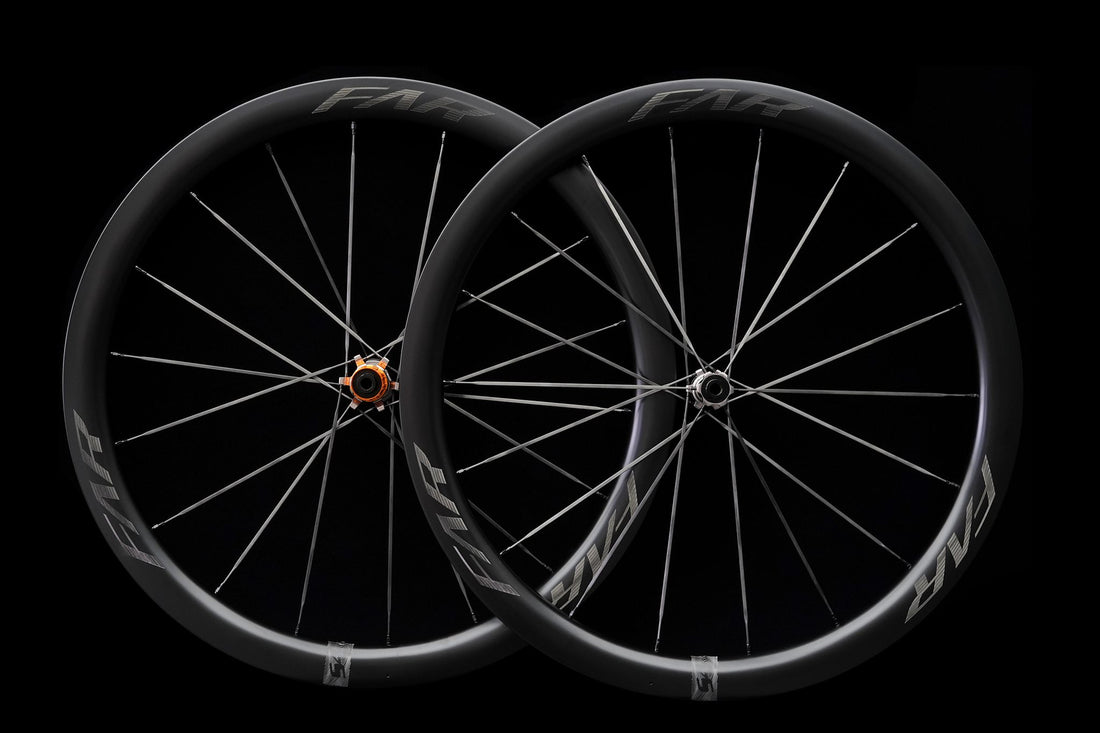 A pair of carbon road wheels on black, the spokes crossing the frame